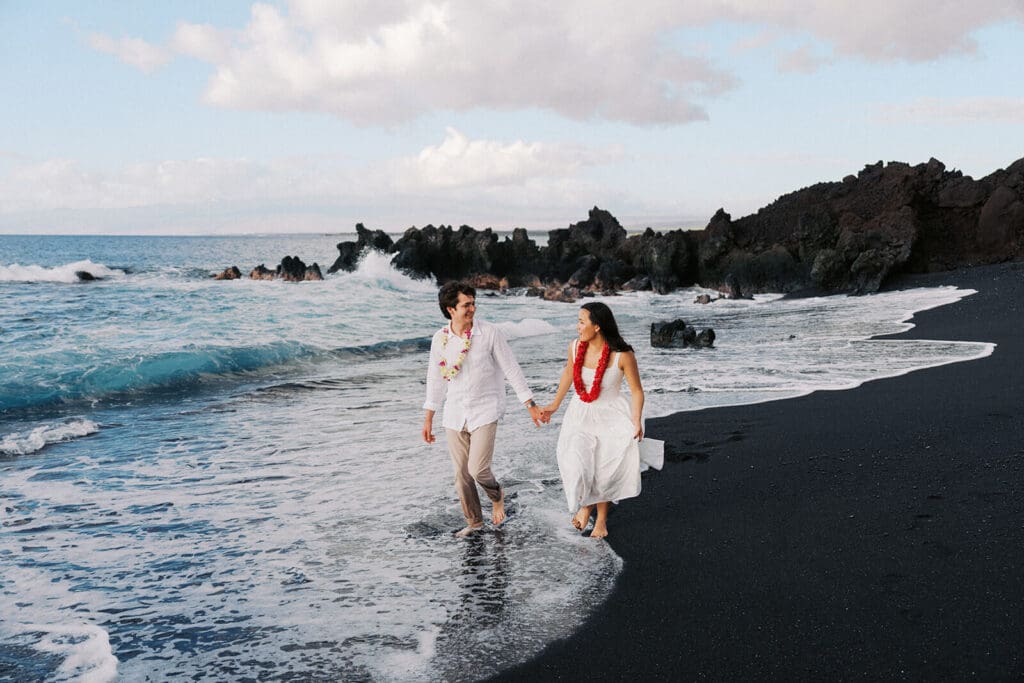 Couple walking hand in hand on secluded black sand beach at Kiholo Bay, Big Island Hawaii