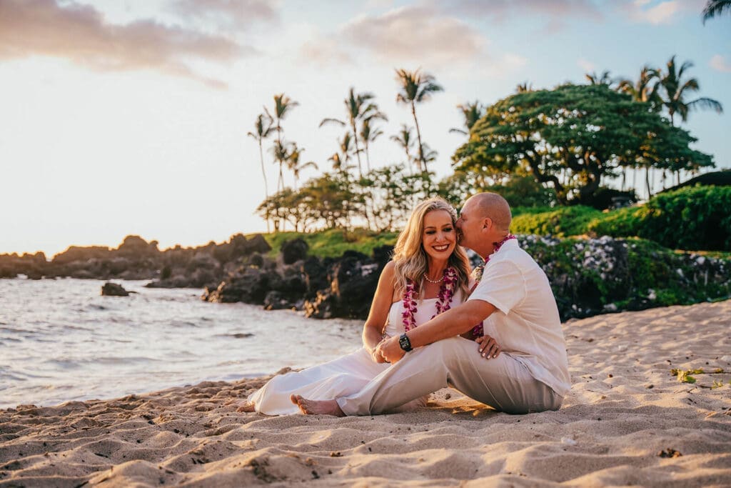 Couple sitting and kissing at Kukio Beach, Big Island Hawaii wedding photography
