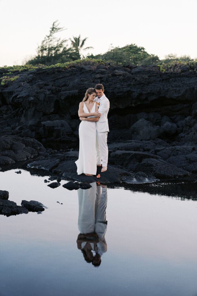 Couple embracing with reflection on Punalu'u Black Sand Beach, Big Island wedding photography