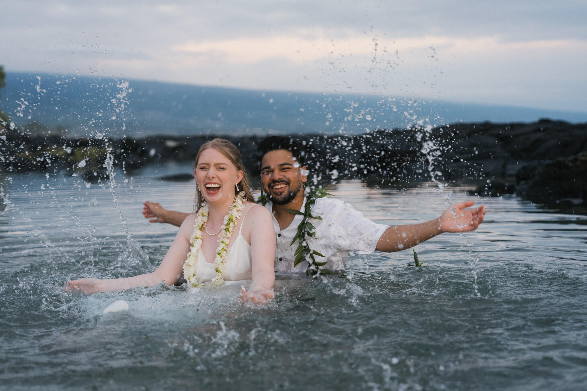 couple splashing and laughing in water during a sunset photo session at old airport beach in Kona