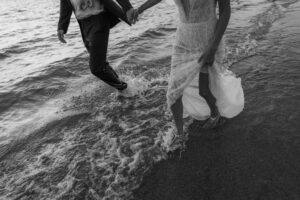 Black and white photo of a bride and groom with their feet in the water at A-Bay Waikaloa